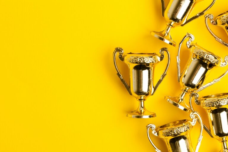 Gold winners trophies on a bright yellow background with space for text